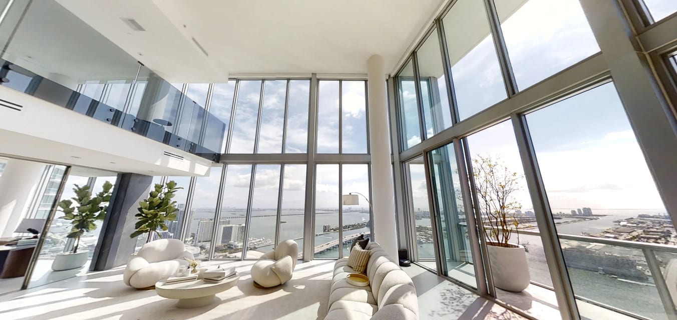 Living de doble altura de un condominio en un piso alto de Miami, con ventanales de piso a techo sobre la bahía de Biscayne